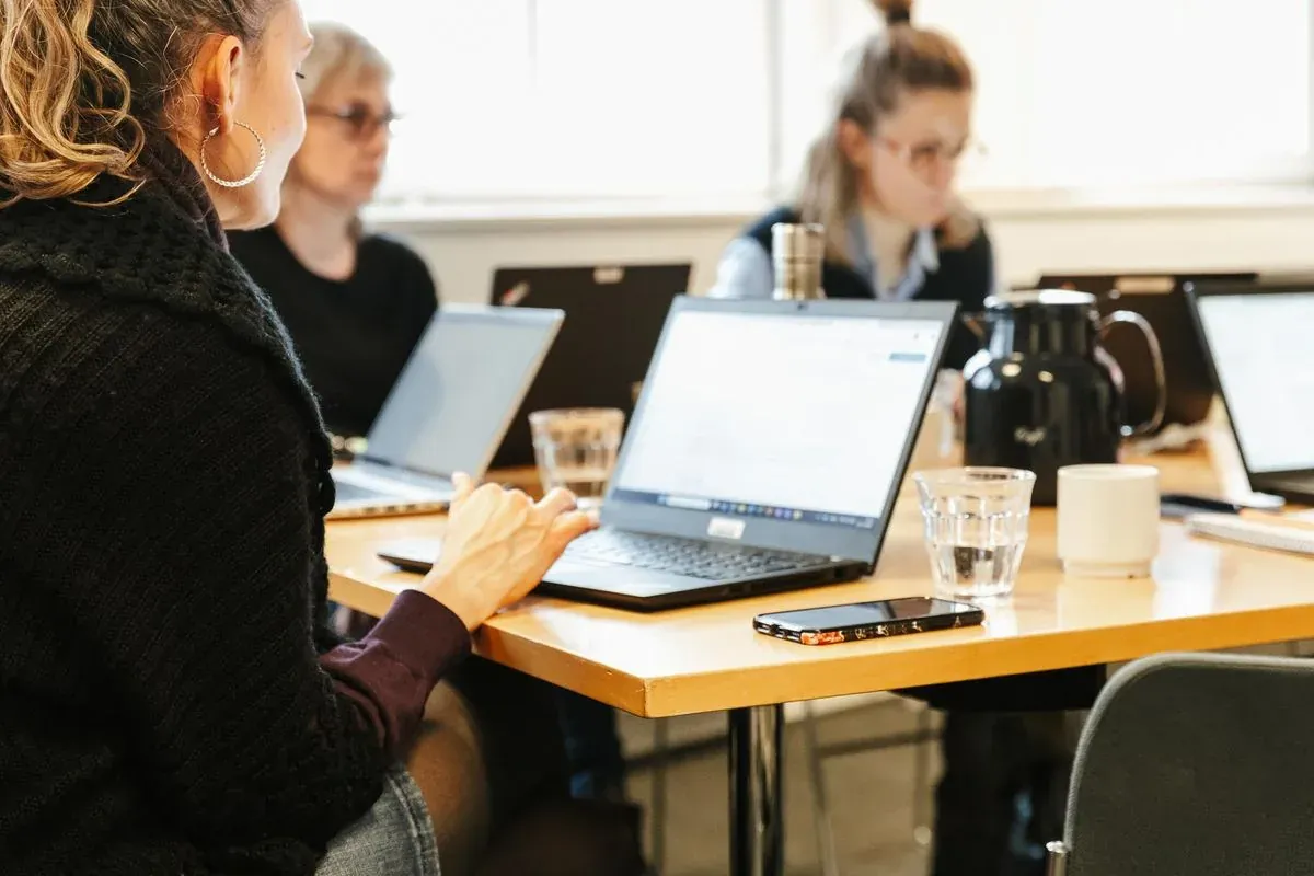 Deltagere arbejder på bærbare computere ved et fælles bord under et kursus.